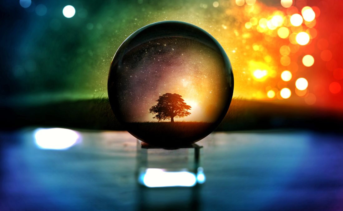 Crystal ball reflecting a tree with rainbow coloured background