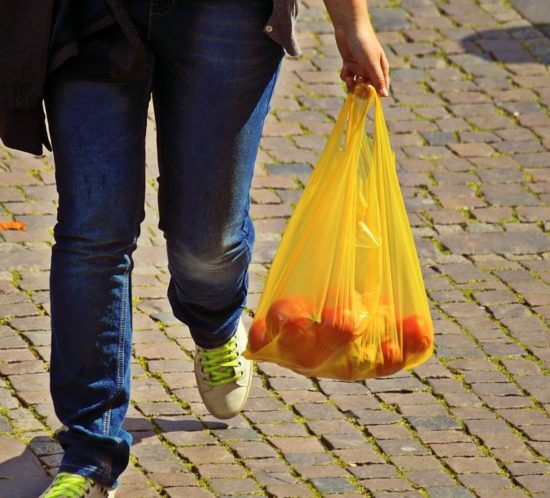 person carrying single use plastic bag filled with oranges