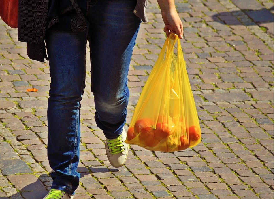 person carrying single use plastic bag filled with oranges